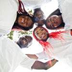Group of happy african volunteers hugs in park. Africa volunteering, charity, people and ecology concept. Look from down.