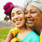 Happy african mother and daughter wearing traditional clothes while having fun together outdoor - Love, travel and family concept - Focus on mum face