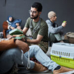 Full length portrait of male volunteer offering food to group of Middle Eastern refugees in shelter, copy space
