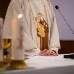 The hands of a catholic priest on altar with candles and microphone for reading a holy book